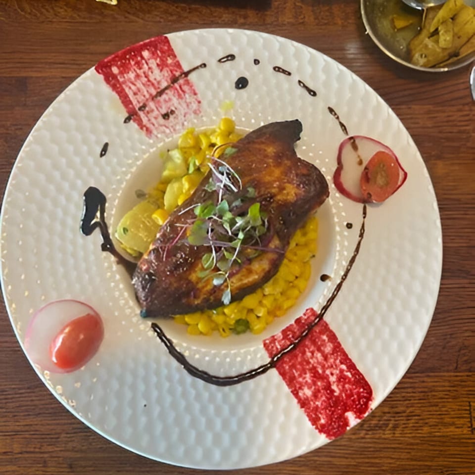 Grilled chicken breast on a bed of corn, garnished with microgreens, radish, and sauce on a white plate.