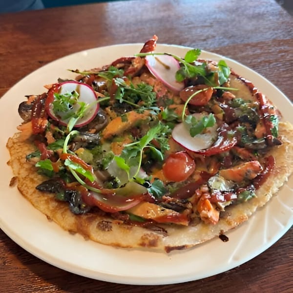 Nepalese flatbread topped with chicken, vegetables, radishes, and a dark sauce on a white plate.
