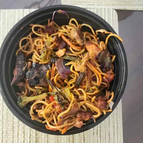 Close-up of Nepalese chowmein noodles with vegetables and meat in a black takeout container.