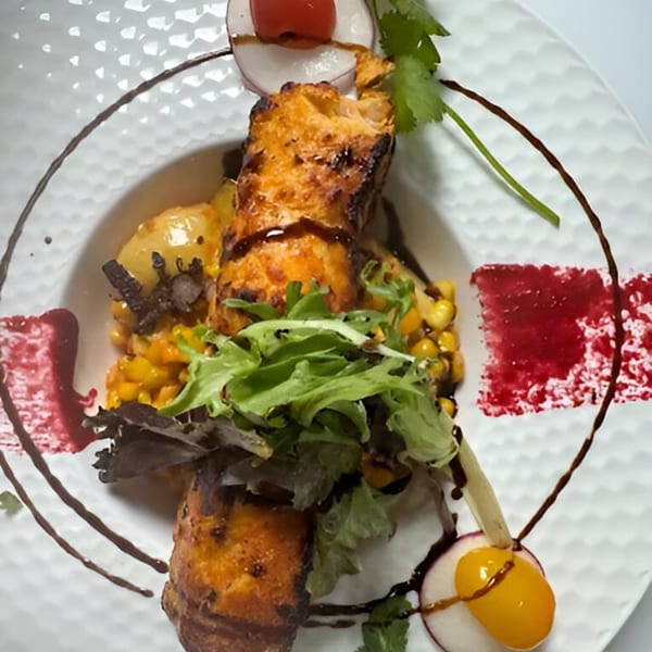 Grilled chicken with corn, potatoes, mixed greens, and balsamic glaze on a white plate.